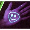 The smiley face on the hand is drawn with a substance containing a phosphor, such as Vasoline (petroleum jelly). Under a black light the phosphors glow.