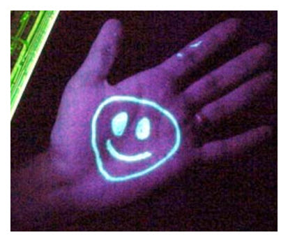 The smiley face on the hand is drawn with a substance containing a phosphor, such as Vasoline (petroleum jelly). Under a black light the phosphors glow.